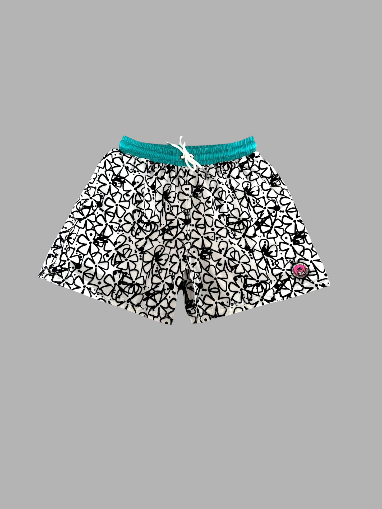 Black and white patterned swim trunks with a teal green elastic waistband and white drawstring, shown against a solid gray background.