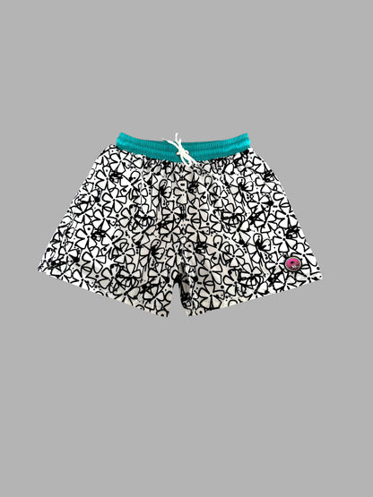 Black and white patterned swim trunks with a teal green elastic waistband and white drawstring, shown against a solid gray background.